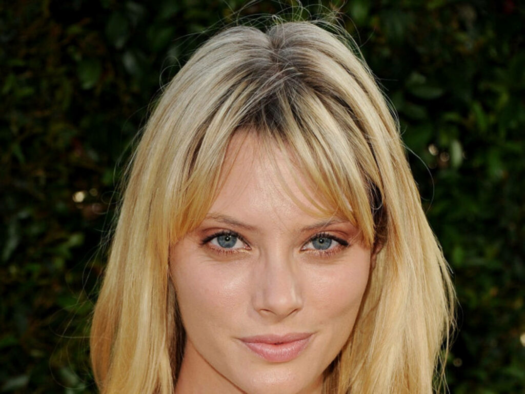 April Bowlby with light brown fringed hair posing outdoors against lush green nature background Wallpaper