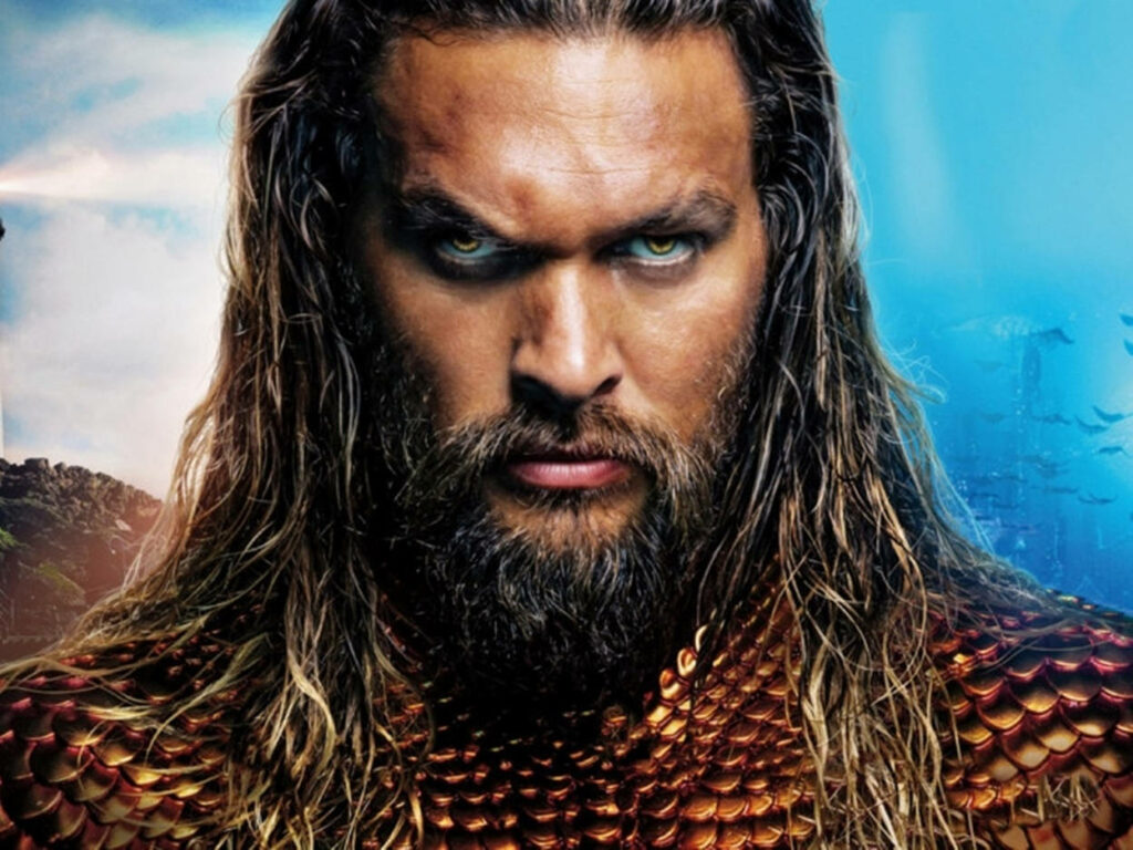 Closeup of Aquaman intense gaze golden armor flowing hair ocean backdrop wallpaper background