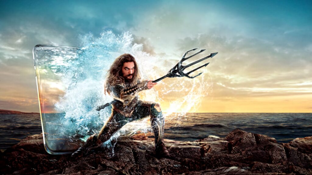 Aquaman rises from ocean waves wielding his trident at sunset dramatic ocean background wallpaper