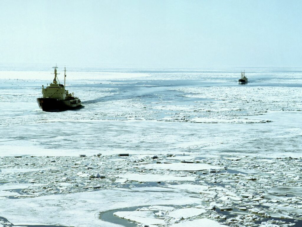 Icebreaker ship breaking thick Arctic ice under frosty sky in frozen ocean landscape wallpaper
