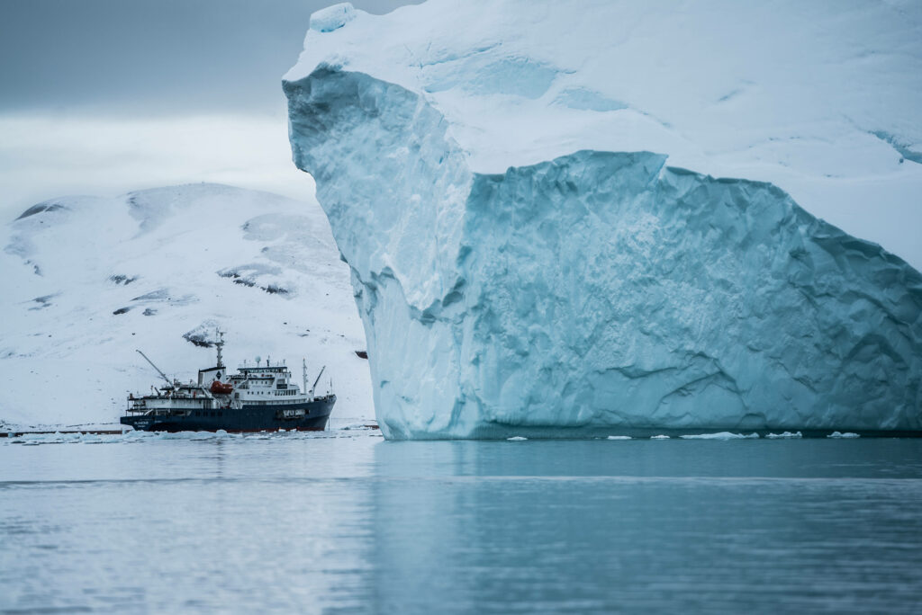 Ship sailing icy Arctic waters near towering Greenland iceberg scenic rugged landscape wallpaper
