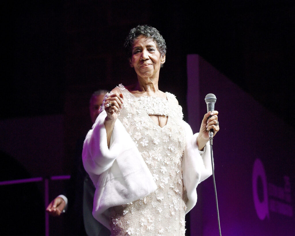 Aretha Franklin captivating audience on stage in elegant dress holding microphone wallpaper background