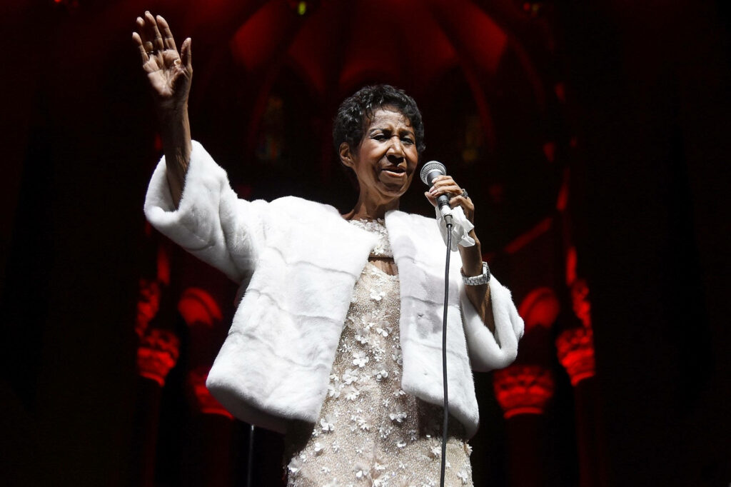 Aretha Franklin performing live in glamorous white outfit under vibrant red stage lighting wallpaper