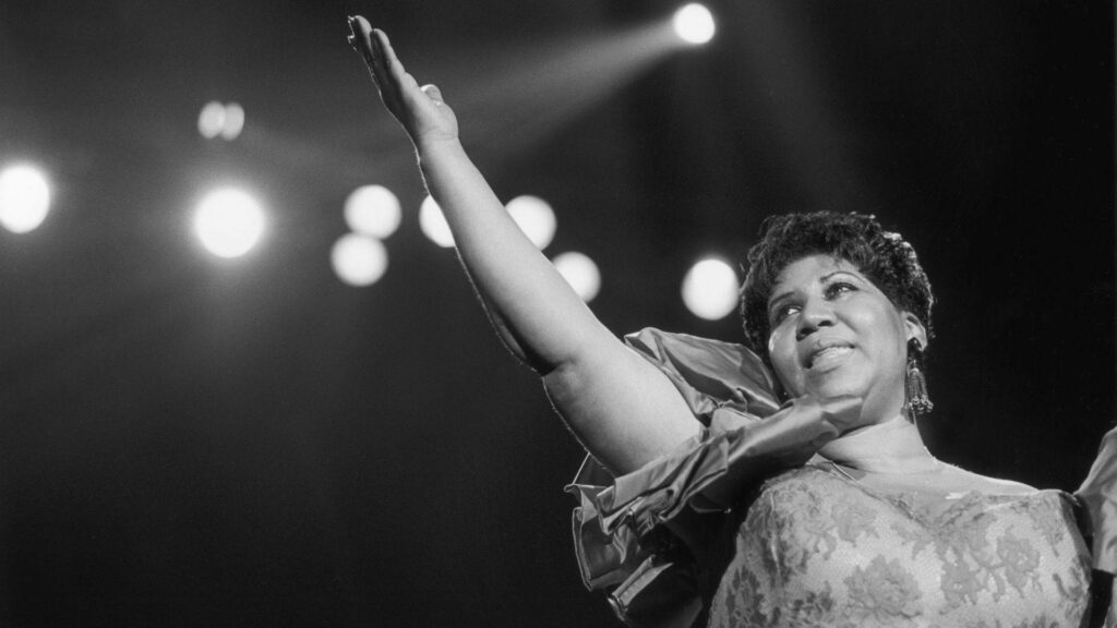 Aretha Franklin singing on stage with arm raised under dramatic lighting iconic American singer Wallpaper