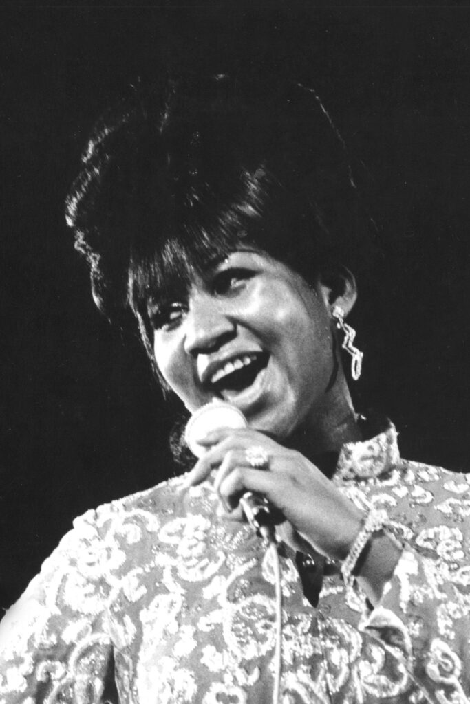 Aretha Franklin performing on stage in elegant patterned outfit holding microphone with soulful energy Wallpaper