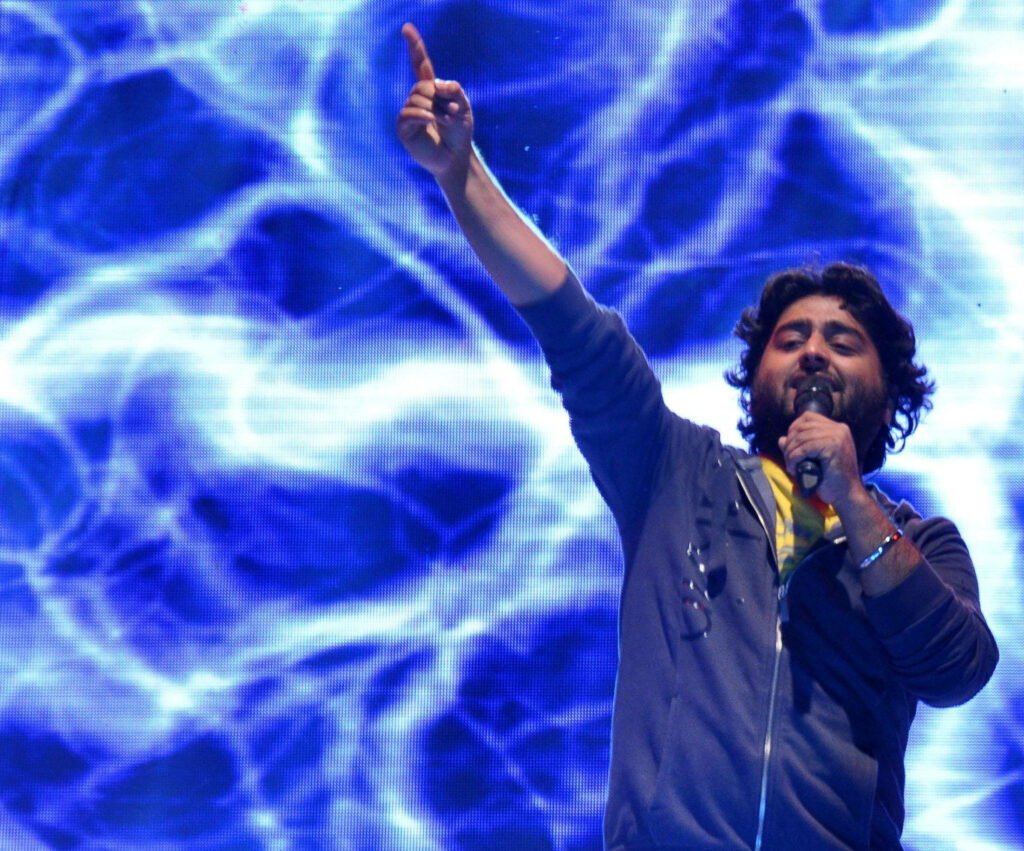 Arijit Singh singing live on stage with vibrant blue abstract backdrop at concert performance Wallpaper