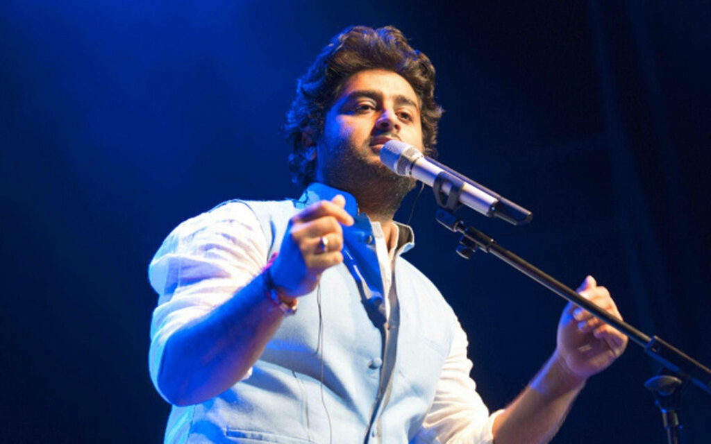 Arijit Singh singing passionately on stage with vibrant blue lighting engaging audience live concert Wallpaper
