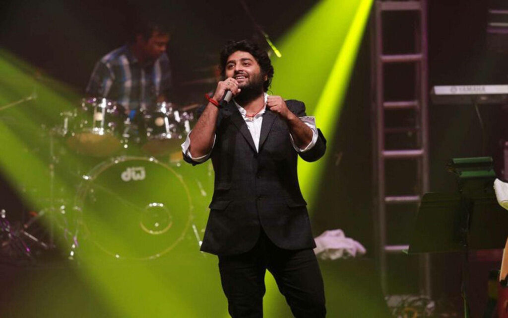 Arijit Singh singing passionately on stage under yellow lights capturing his melodious voice Wallpaper