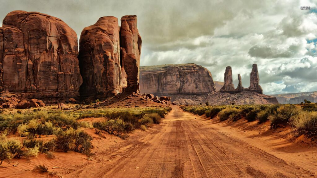 Long dirt path through Arizona desert with red rock formations and dramatic cloudy sky wallpaper