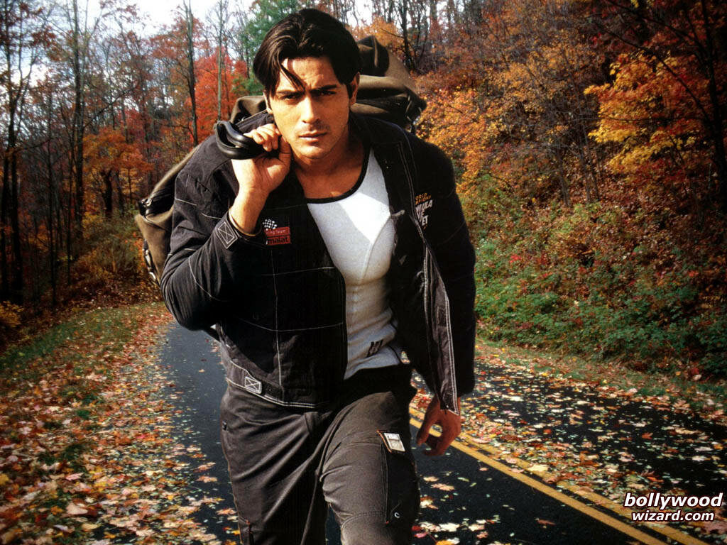 Arjun Rampal stylishly walking on autumn leaf-covered road with vibrant fall trees background Wallpaper