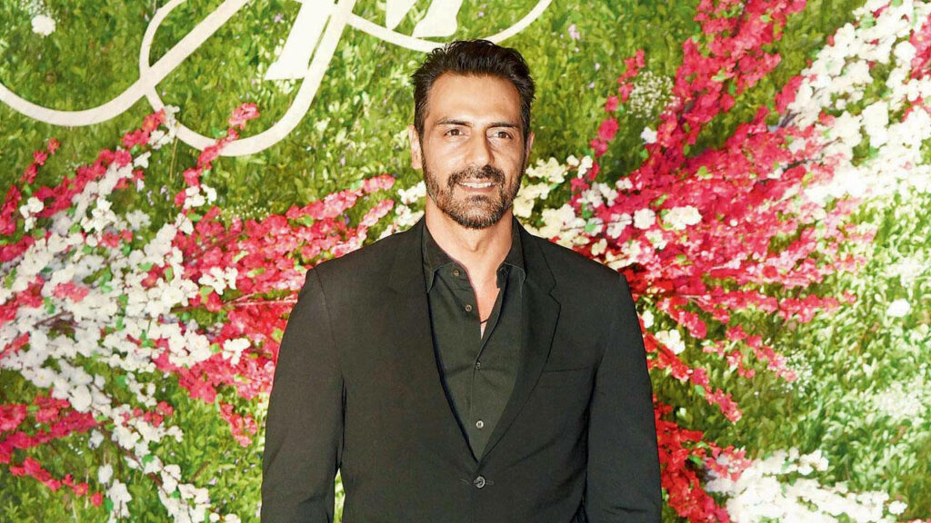Arjun Rampal in black suit stands confidently with vibrant floral wallpaper background