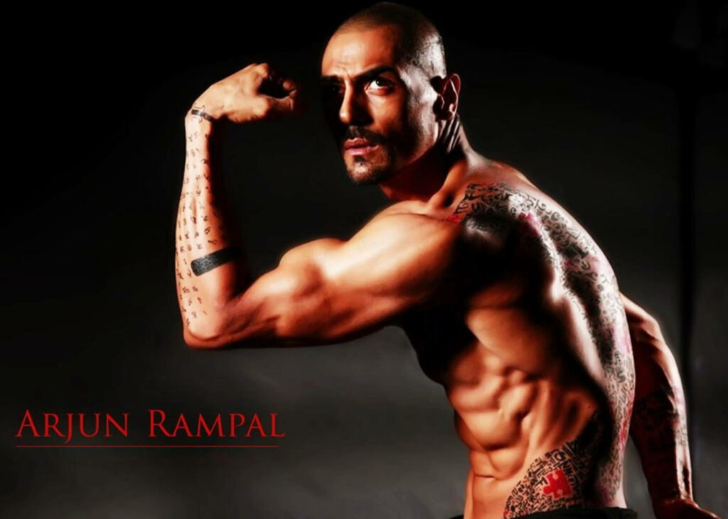 Arjun Rampal flexing muscles and tattoos in intense pose dark background wallpaper image