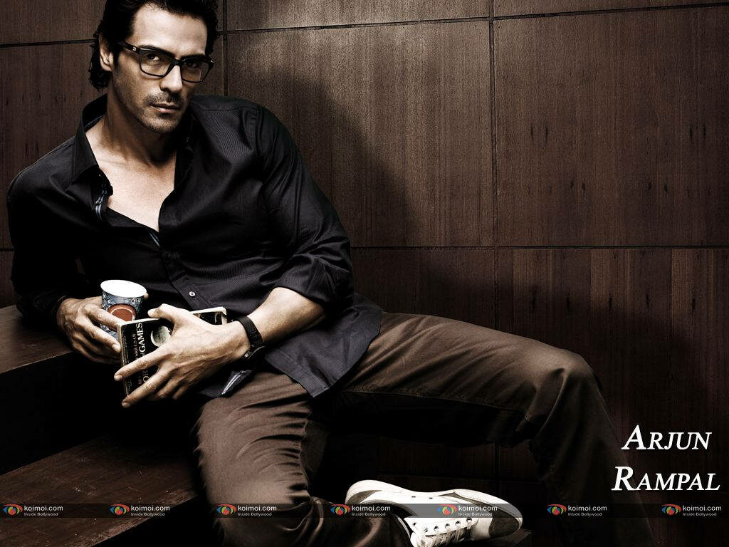 Bollywood star Arjun Rampal sitting thoughtfully with coffee cup against wooden wall background Wallpaper