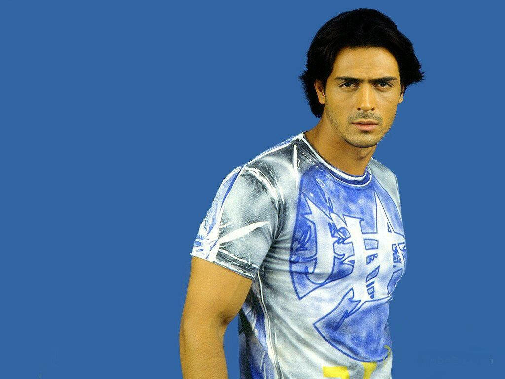 Arjun Rampal confident pose in stylish graphic t-shirt against solid blue wallpaper background