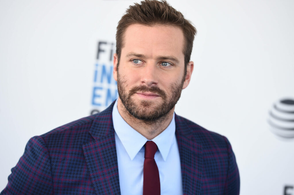 Armie Hammer in sharp plaid suit red tie posing at 2019 FISA event white wallpaper background