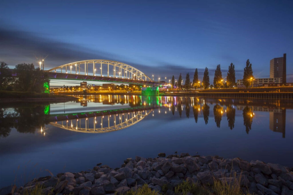Arnhem Bridge glowing at night with city lights reflected in calm water scenic wallpaper background