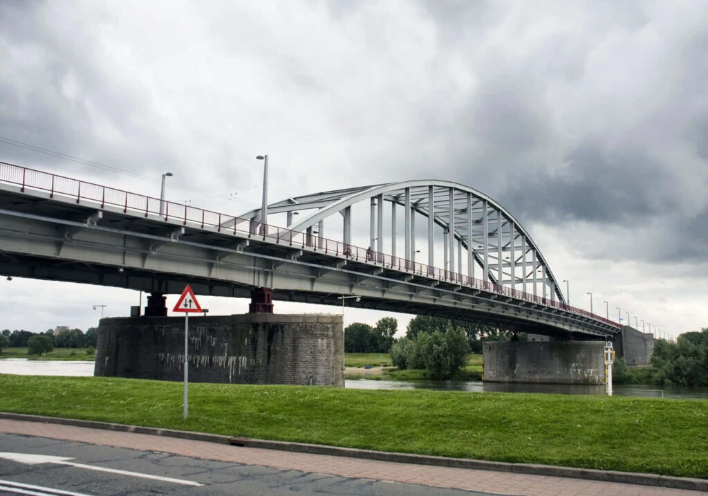 Arnhem Bridge over river with lush green grass and dramatic cloudy sky wallpaper background