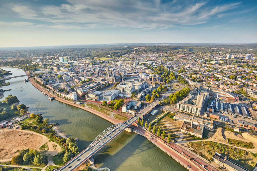 Aerial view of Arnhem city with iconic bridge historic buildings lush greenery and blue sky Wallpaper