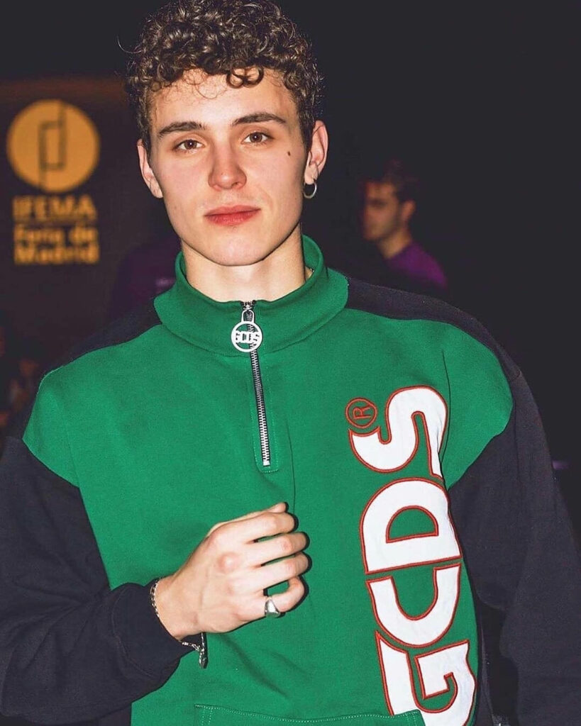 Arón Piper wearing green GCDS jacket confidently posing in stylish bold fashion wallpaper background
