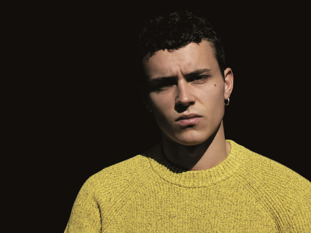 Arón Piper wearing yellow sweater against dark background Spanish actor wallpaper background