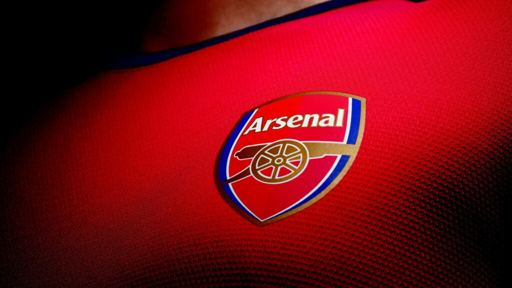 Arsenal FC breastplate logo on red jersey fabric emphasizing football club pride wallpaper