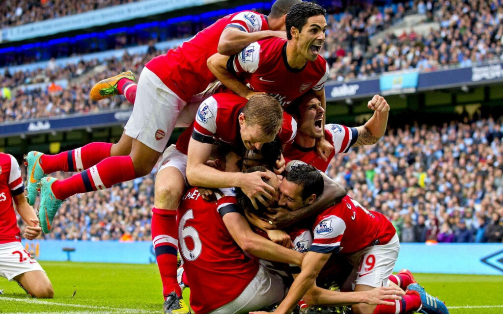 Arsenal FC players celebrate passionately on field after thrilling victory capturing team unity Wallpaper