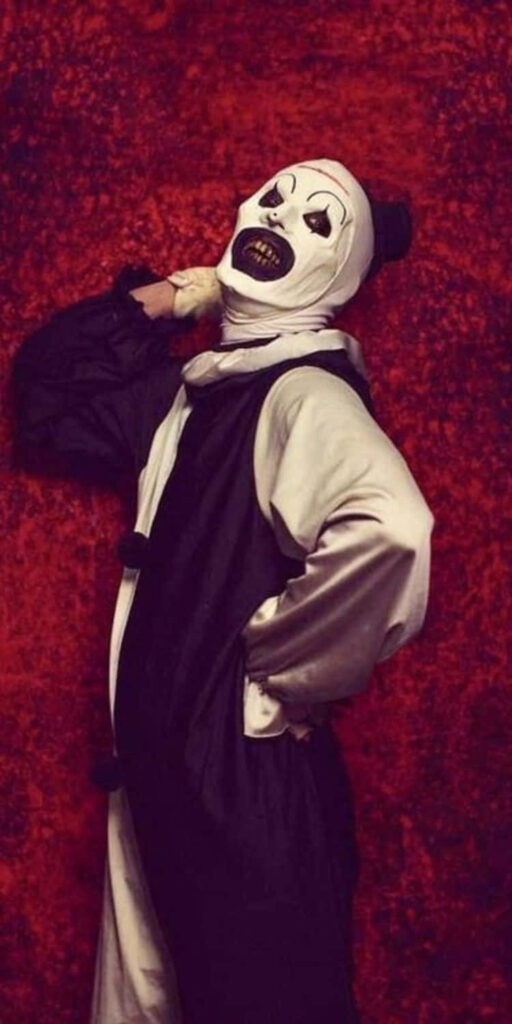 Art The Clown from Terrifier in chilling pose against vivid red horror wallpaper background