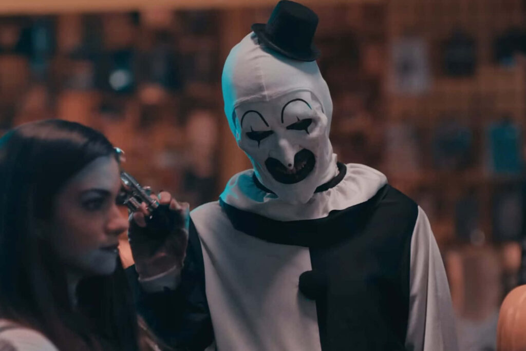Art The Clown menacingly points gun at woman in intense Terrifier horror scene wallpaper background