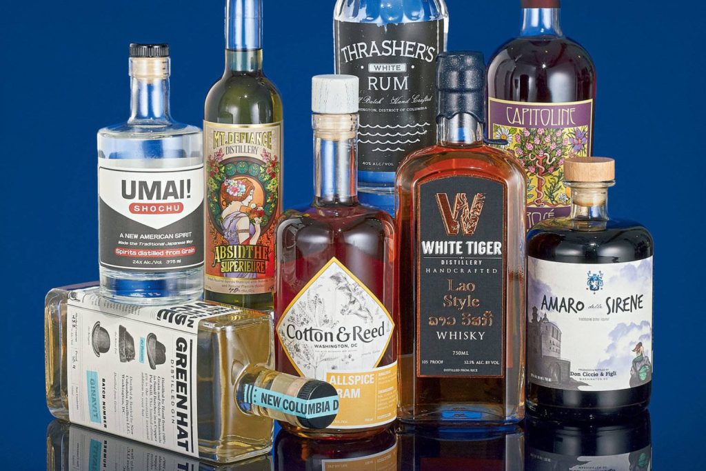 Curated artisan spirits collection with Green Hat Gin White Tiger Whisky Amaro against blue background Wallpaper