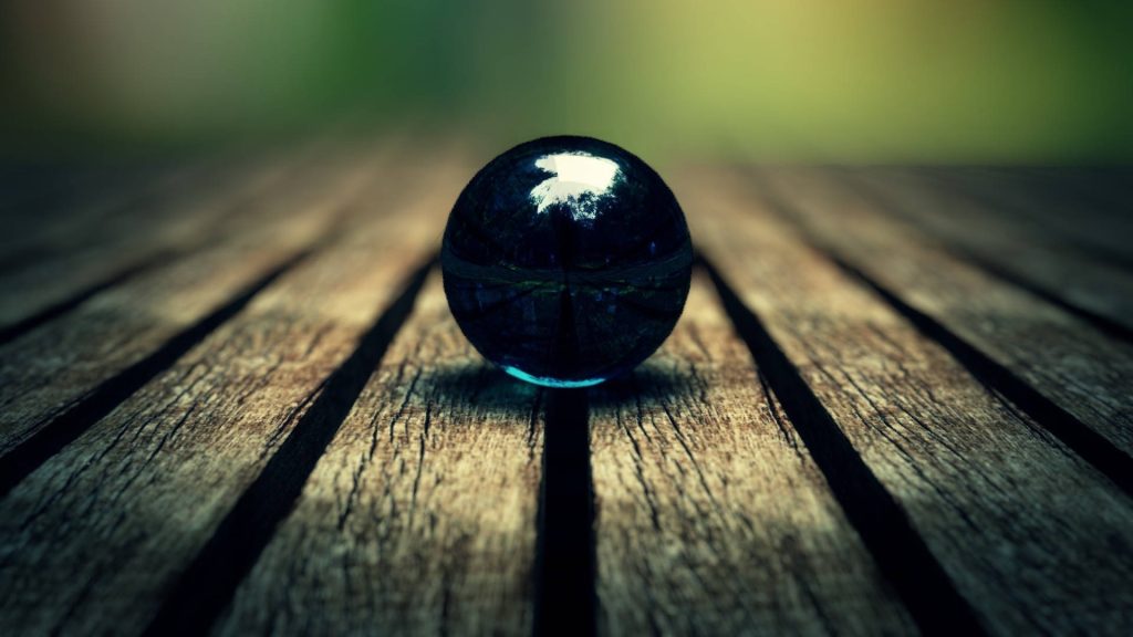Polished glass sphere on rustic wood with moody lighting and blurred black marble background wallpaper