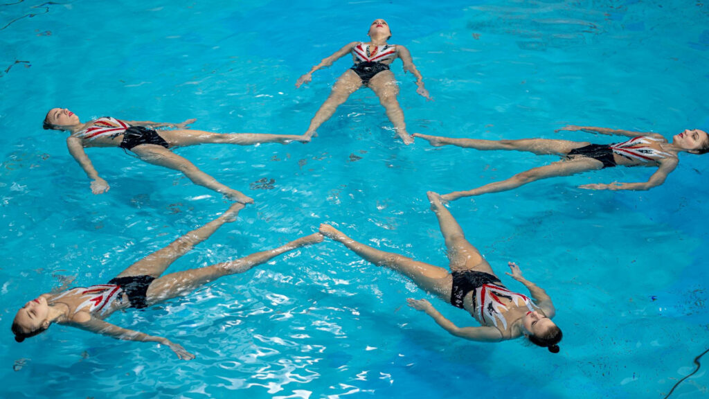 Artistic swimmers forming a star pattern in vibrant blue pool demonstrating synchronization Wallpaper