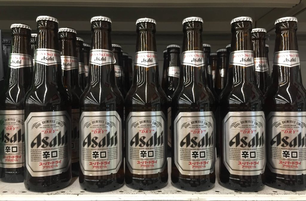 Asahi Super Dry beer bottles lined up on shelf with silver white labels in high resolution Wallpaper