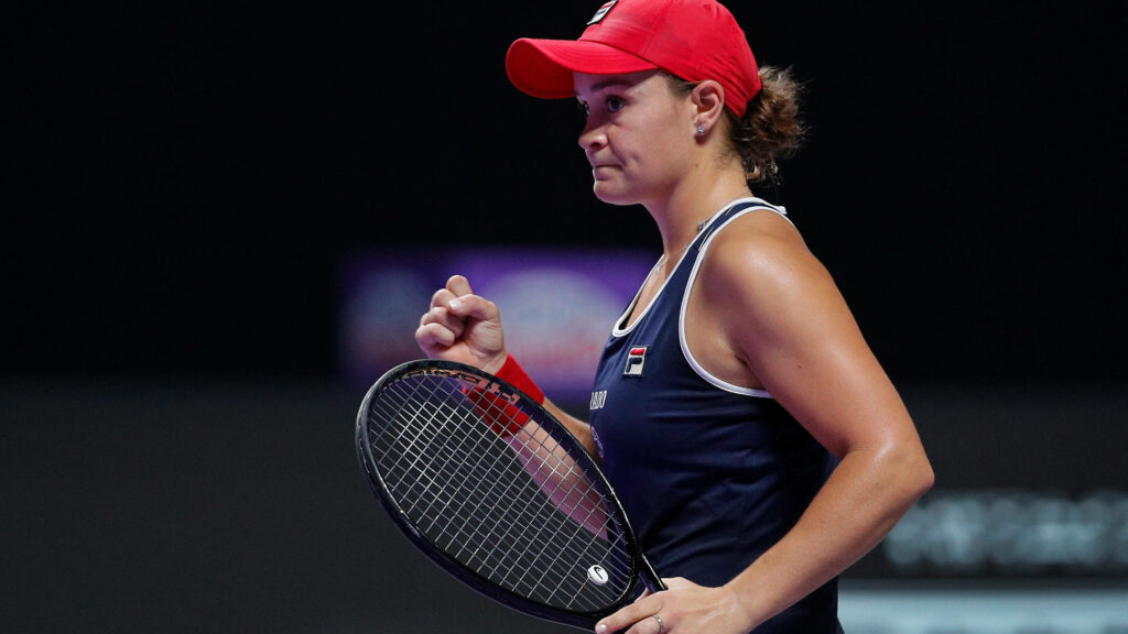 Ashleigh Barty in red cap focused playing tennis with racket on court against wallpaper background