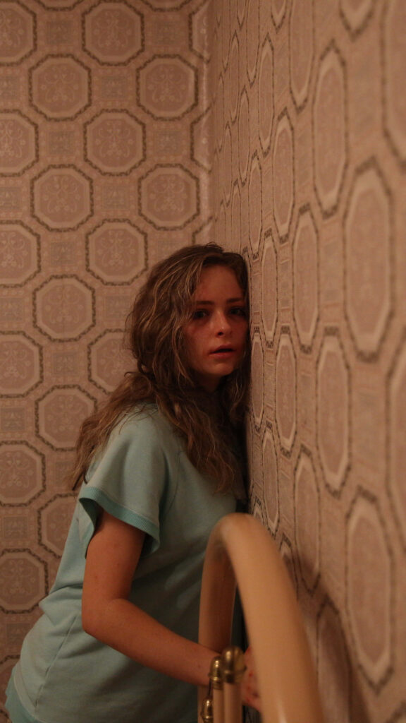 Ashleigh Cummings thoughtful pose against vintage patterned wallpaper evoking quiet introspection