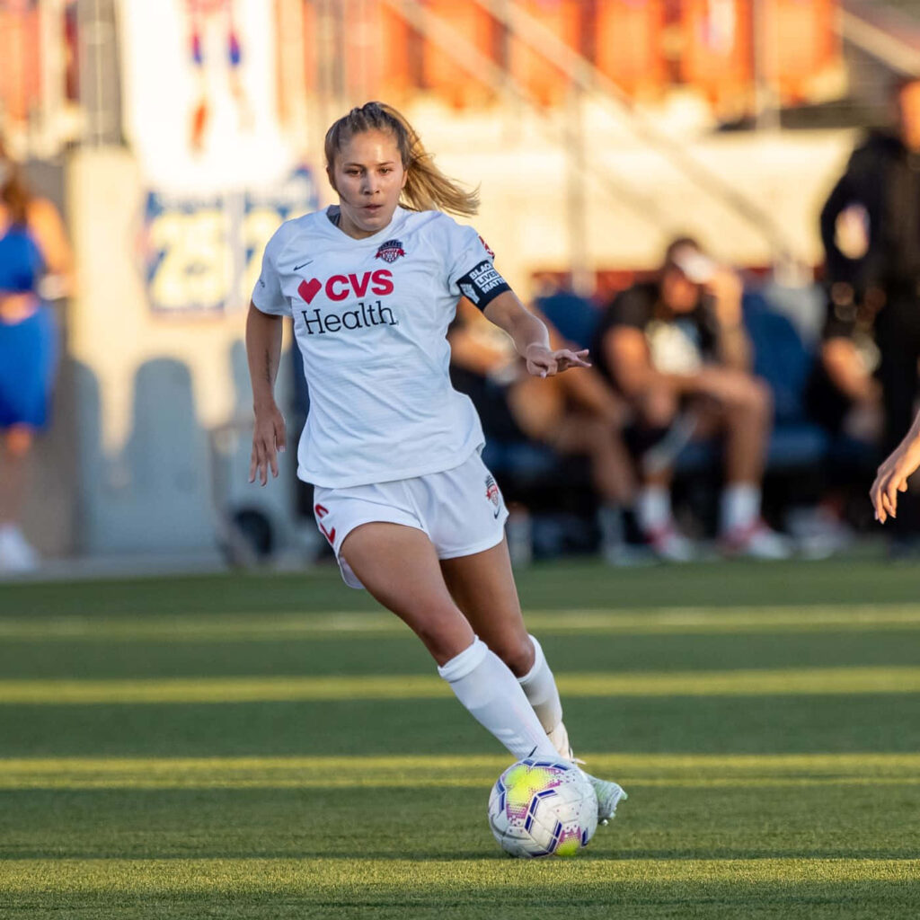 Ashley Sanchez controlling soccer ball focused in white team kit during intense match play Wallpaper