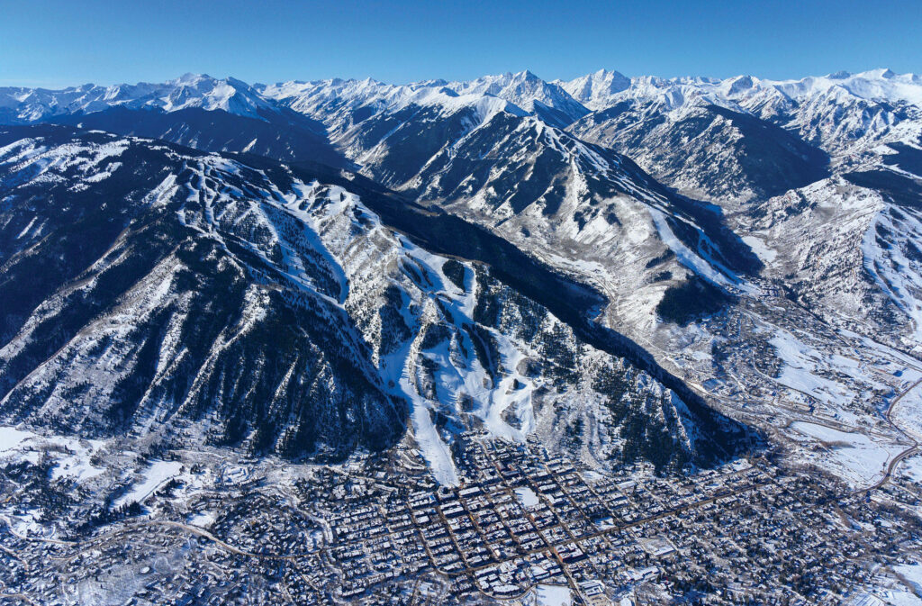 Aerial view of snow-covered Aspen Colorado mountains ski slopes and charming town under blue sky Wallpaper