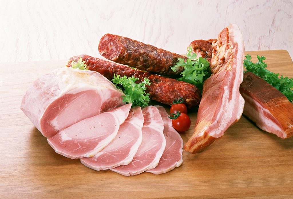 Assorted cured meats sliced ham sausages bacon on rustic board with lettuce cherry tomatoes Wallpaper