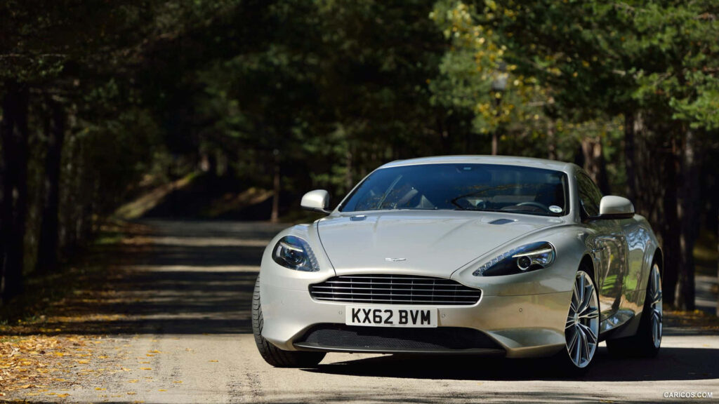Aston Martin DB9 luxury sports car driving on scenic tree-lined road wallpaper background