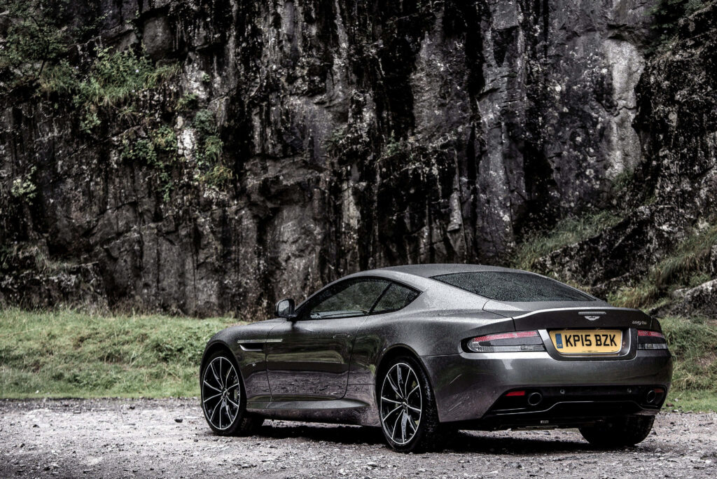 Aston Martin DB9 parked by rugged rocks showcasing sleek design and dynamic luxury car wallpaper