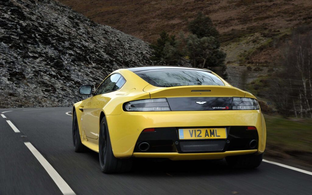 Aston Martin V12 Vantage driving on winding mountain road showcasing luxury performance wallpaper