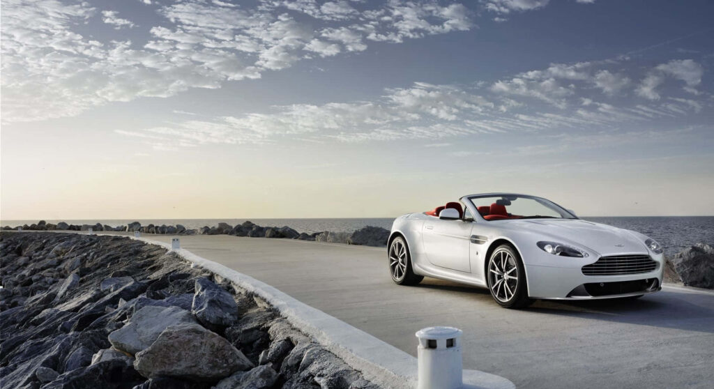 Aston Martin V12 Vantage sleek design parked by tranquil seaside showcasing dynamic presence Wallpaper