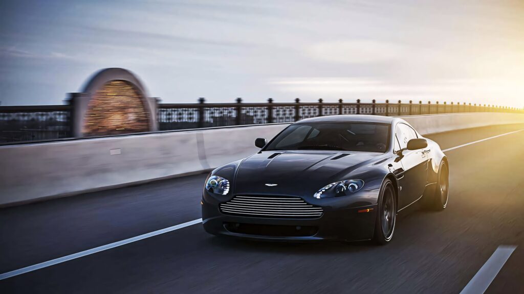 Aston Martin V12 Vantage speeding on open road at sunset sleek design powerful performance wallpaper