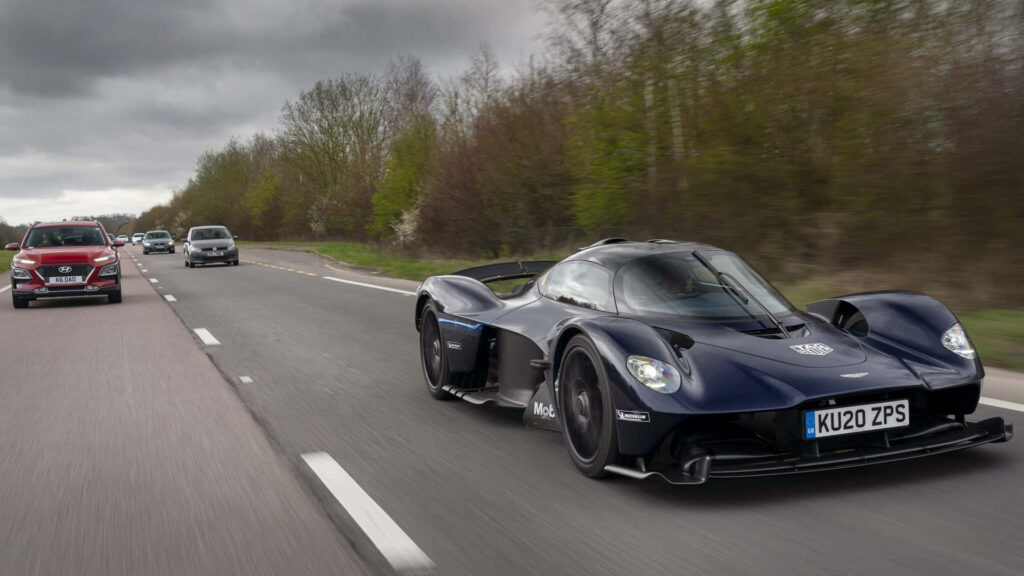 Aston Martin Valkyrie hypercar leading a convoy on open road under cloudy sky wallpaper background