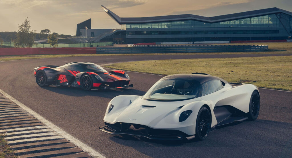 Aston Martin Valkyrie hypercar with two models on racetrack near modern building showcasing design Wallpaper