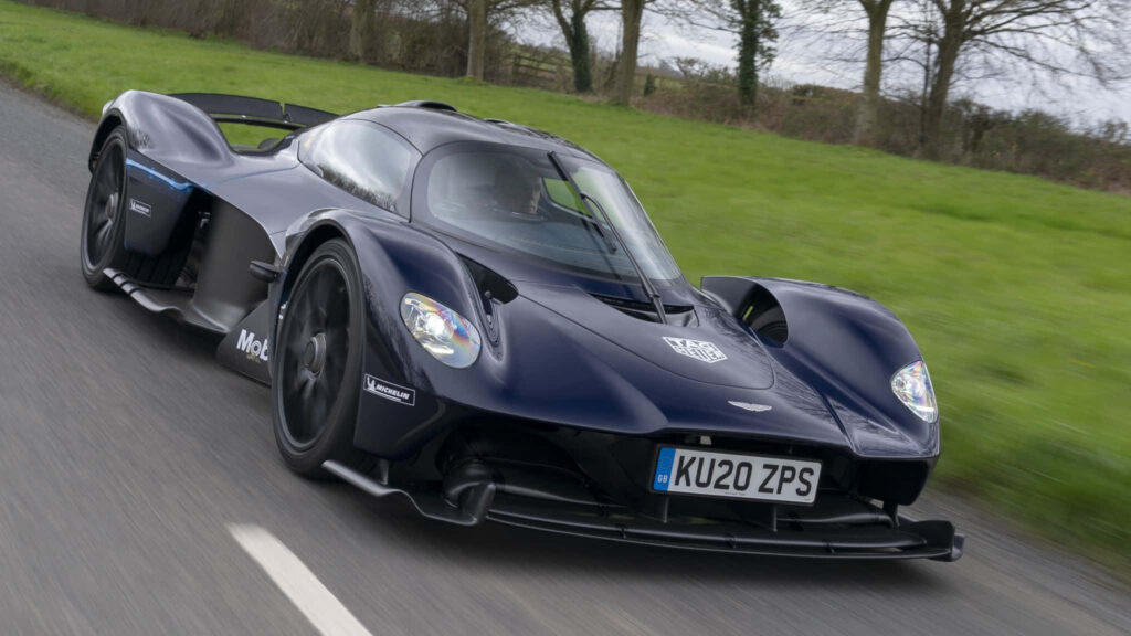 Aston Martin Valkyrie racing on highway with green fields and open skies speed wallpaper background