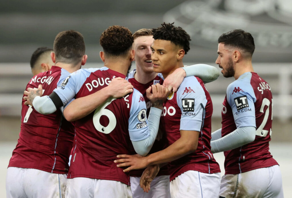 Aston Villa players in claret and blue kits huddle showing team unity and determination on pitch Wallpaper