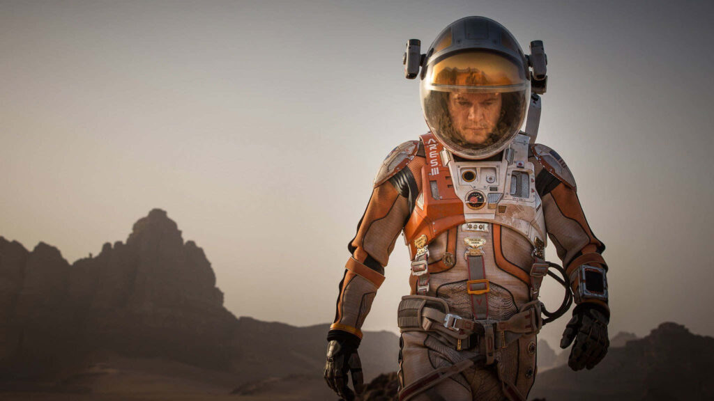 Astronaut Mark Watney trekking rugged Martian terrain in space suit survival determination wallpaper