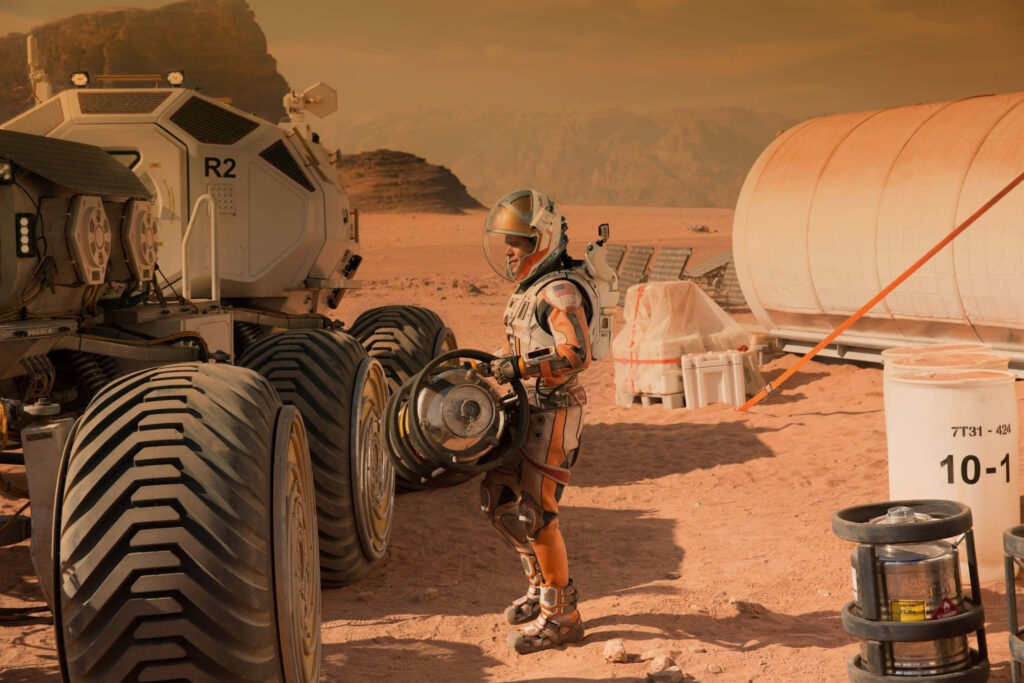Astronaut Mark Watney on Mars near rover preparing equipment in rugged Martian landscape wallpaper
