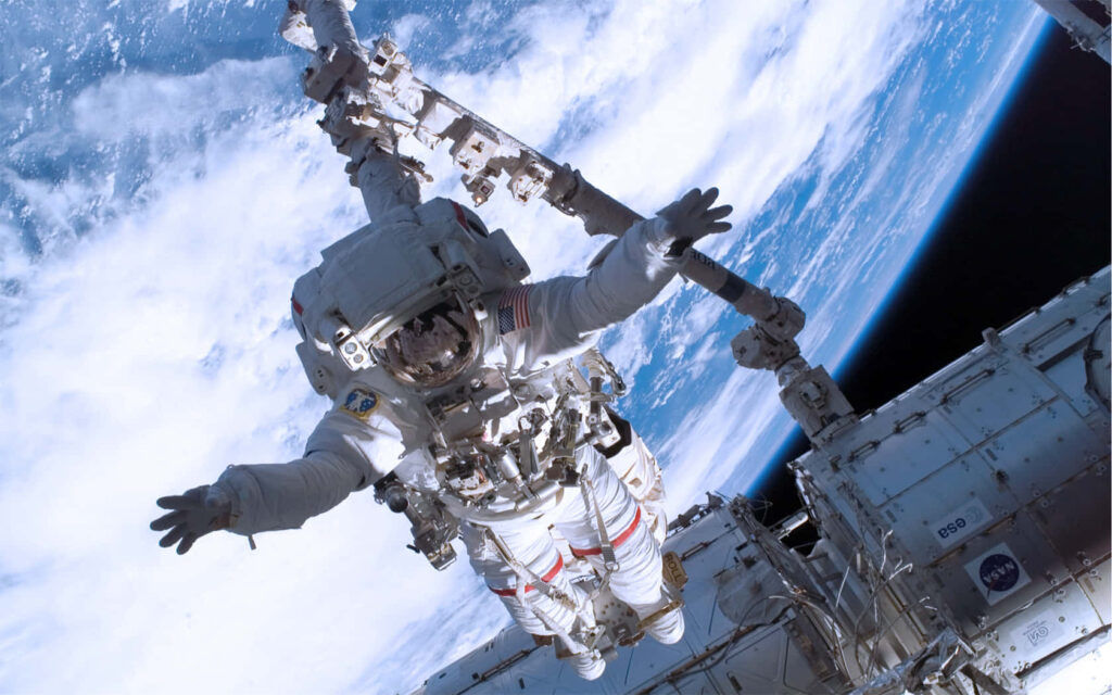 Stunning Astronaut Wallpaper: ISS Orbiting Earth with Blue Atmosphere