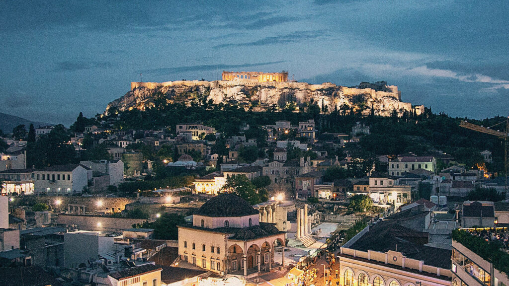 Grainy dusk view of Athens with illuminated Acropolis and historic city buildings below wallpaper